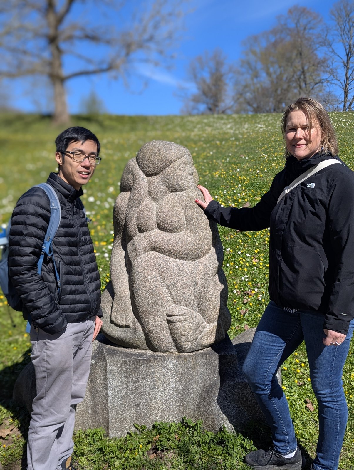 Daiga e un ospite accanto alla scultura della madre con bambino seduta alla Collina delle Daine, Turaida