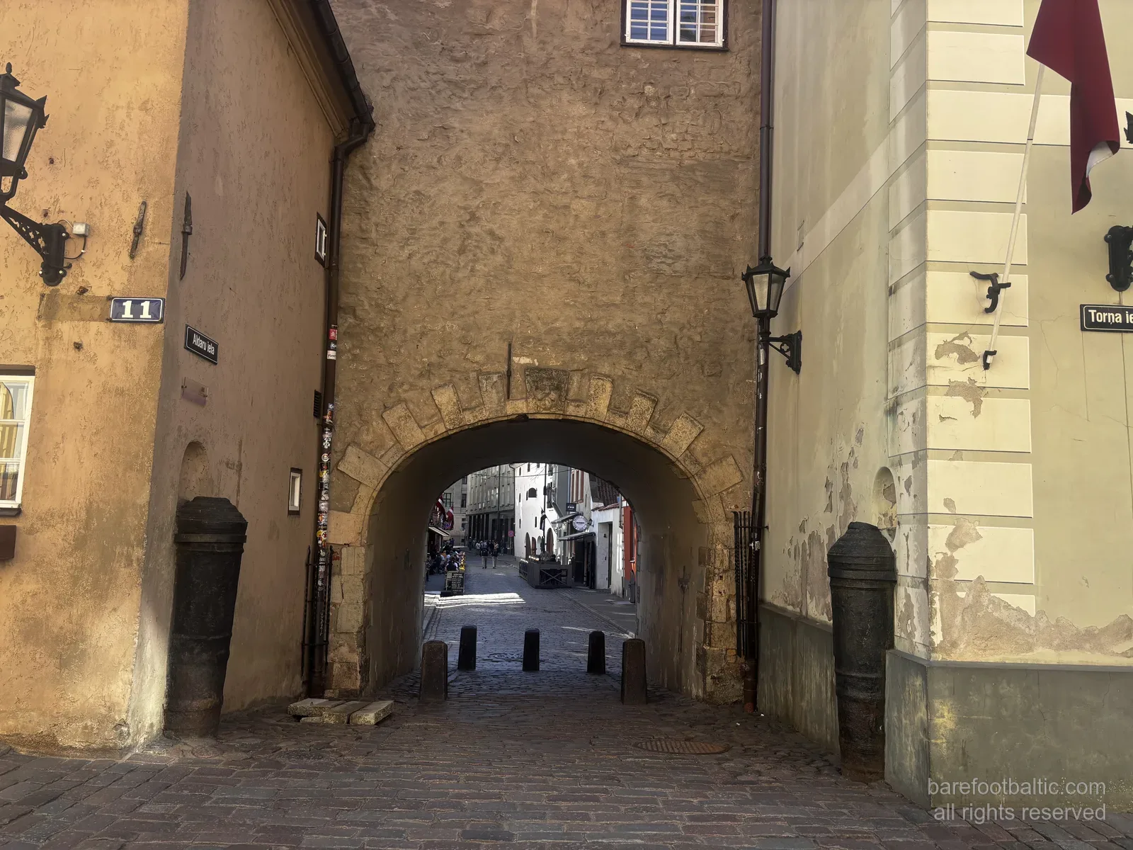 La Porta Svedese (Zviedru vārti) su Torņa iela nella Città Vecchia di Riga, Lettonia, un arco di pietra tra due edifici gialli.