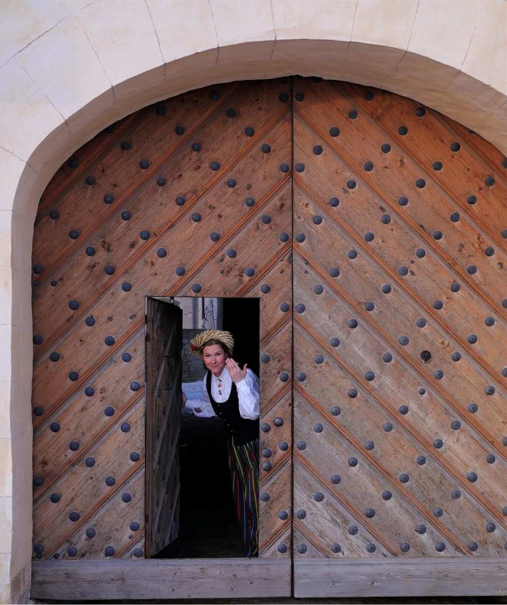 Daiga in costume popolare lettone tradizionale che fa capolino dal portone di legno borchiato del Palazzo di Rundāle