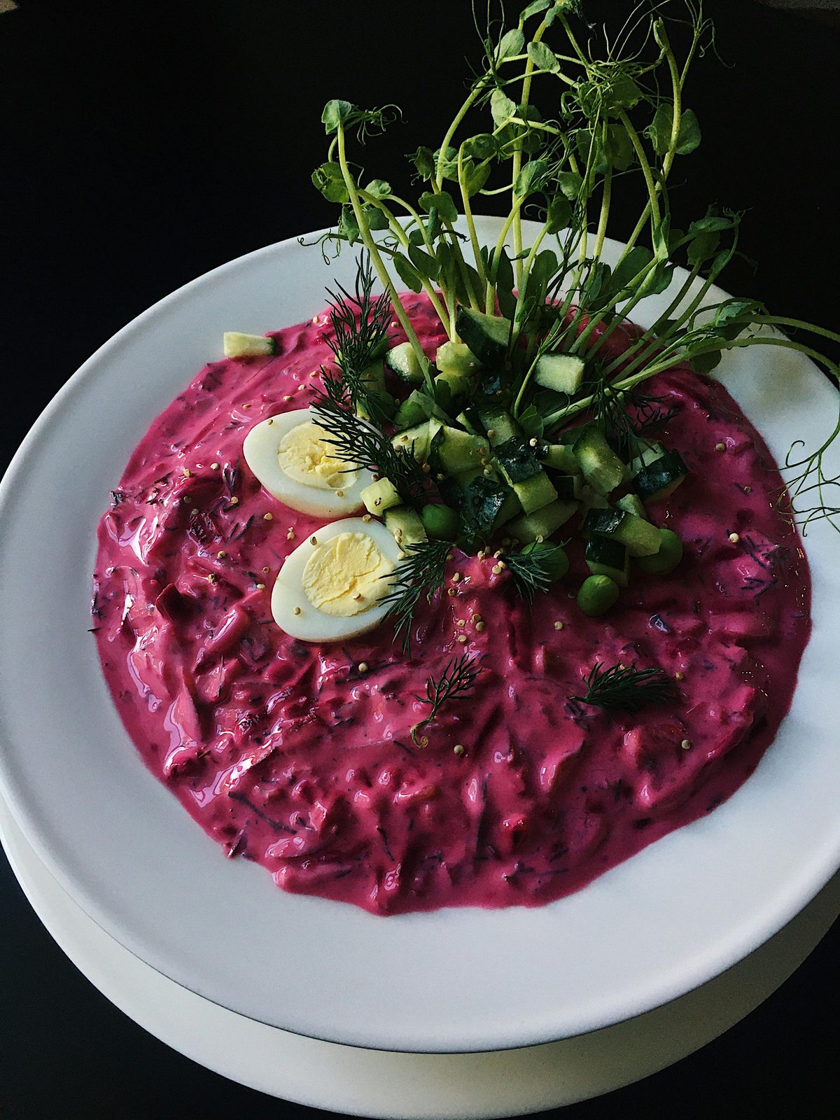 Una ciotola di aukstā zupa rosa acceso, la zuppa estiva fredda lettone a base di kefir e barbabietola, guarnita con uovo sodo, cetriolo e aneto