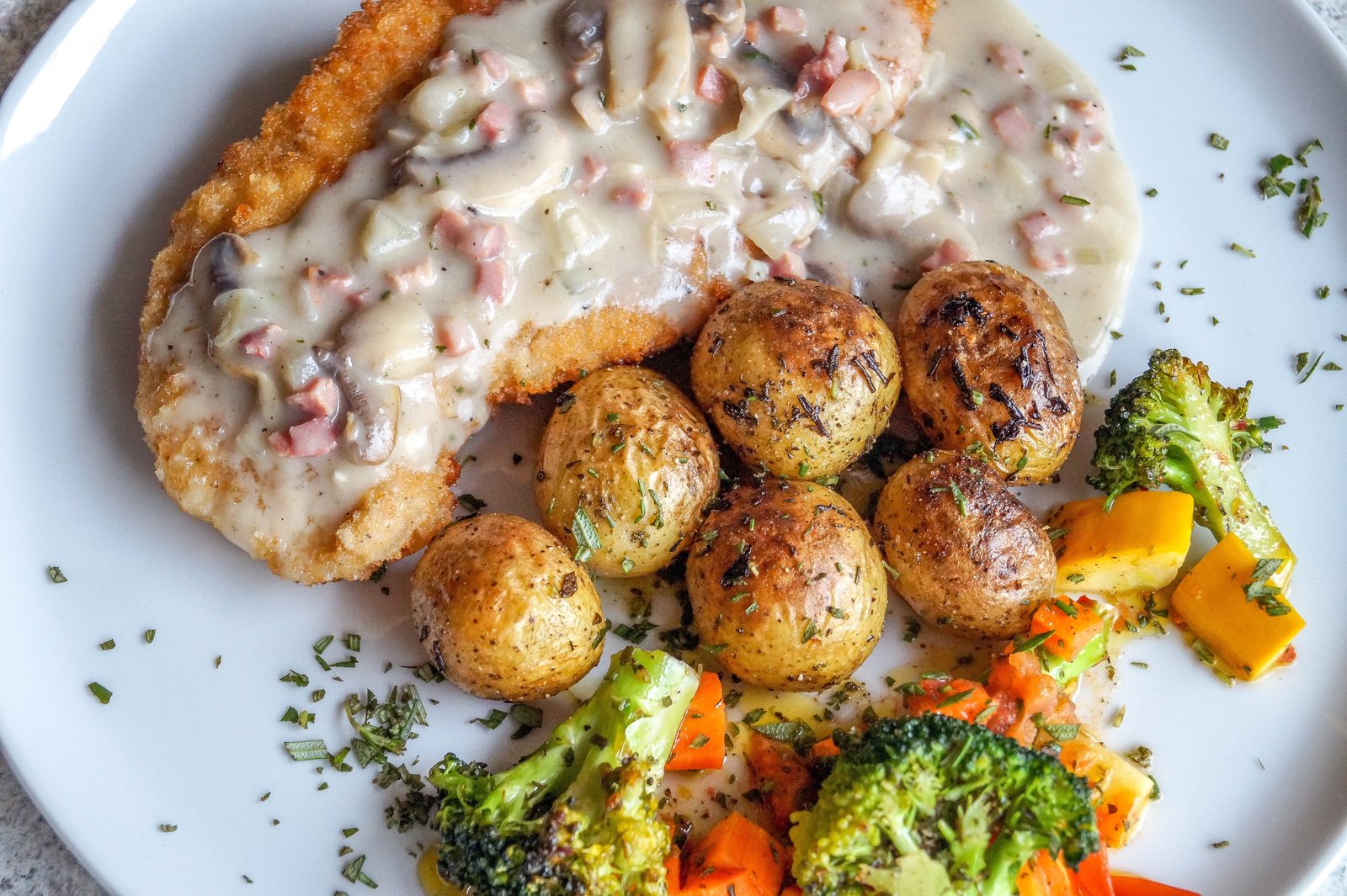 Un piatto di karbonāde, cotoletta di maiale impanata lettone, con salsa cremosa ai funghi, patate alle erbe e verdure arrostite