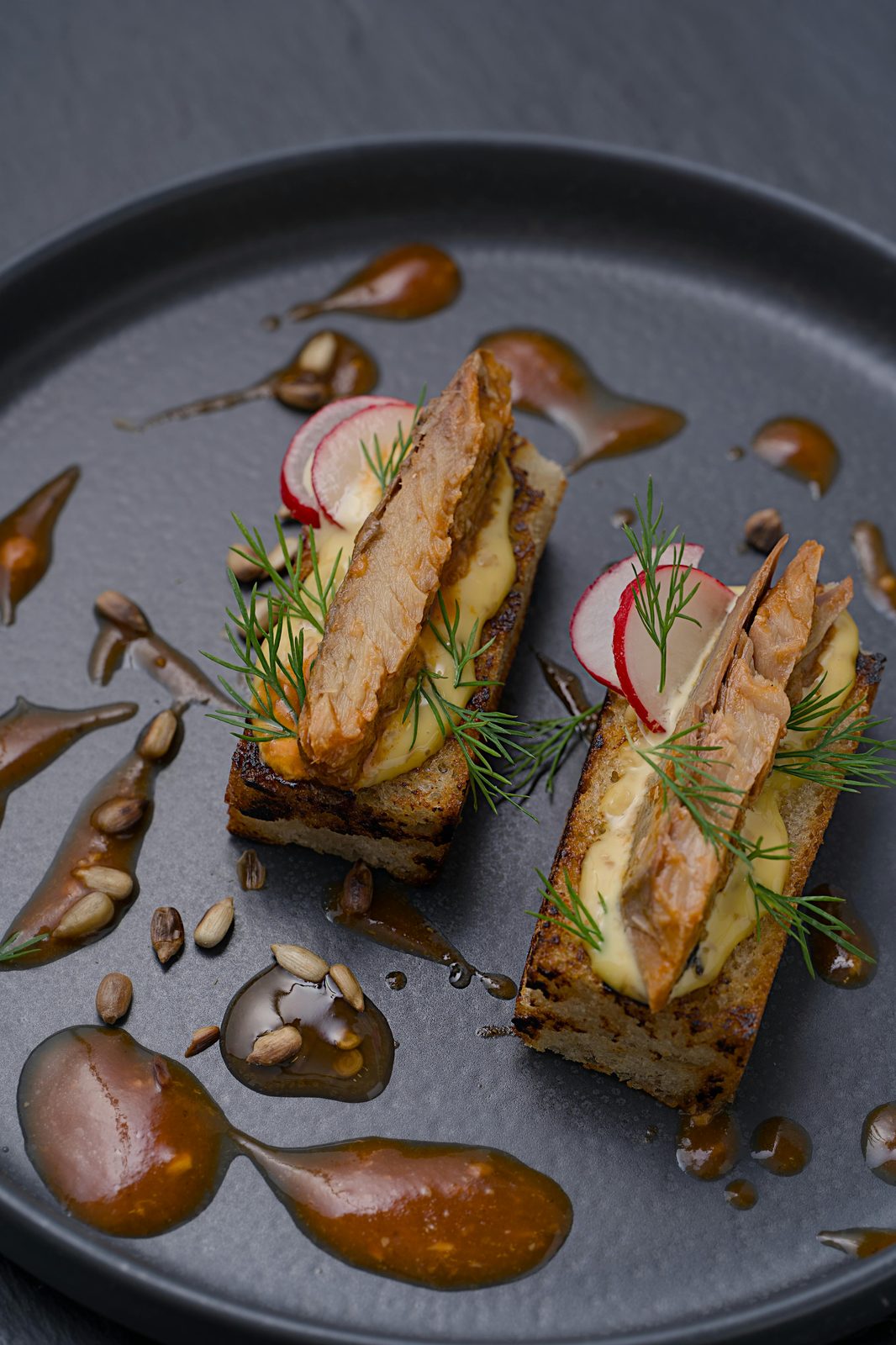 Antipasto di pesce affumicato su segale tostata con panna, aneto e ravanello, servito su un piatto nero