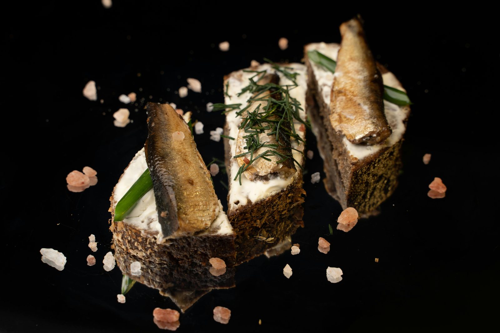 Tre spratti affumicati su pane di segale con panna acida e aneto, su sfondo nero
